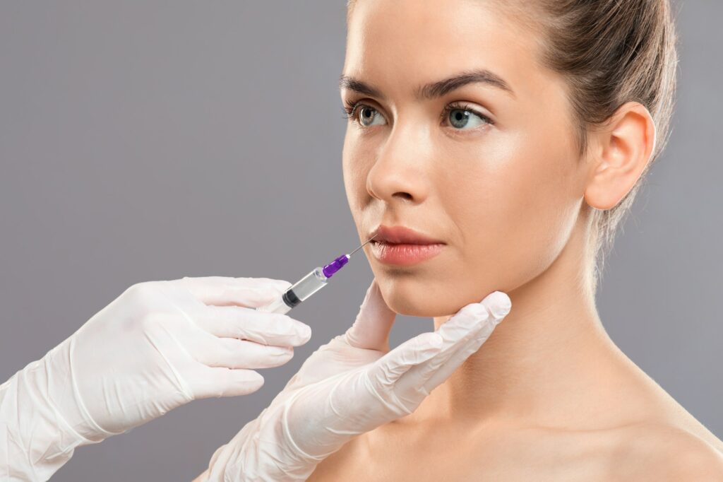 Unrecognizable cosmetitian in gloves injecting lip filler for beautiful lady